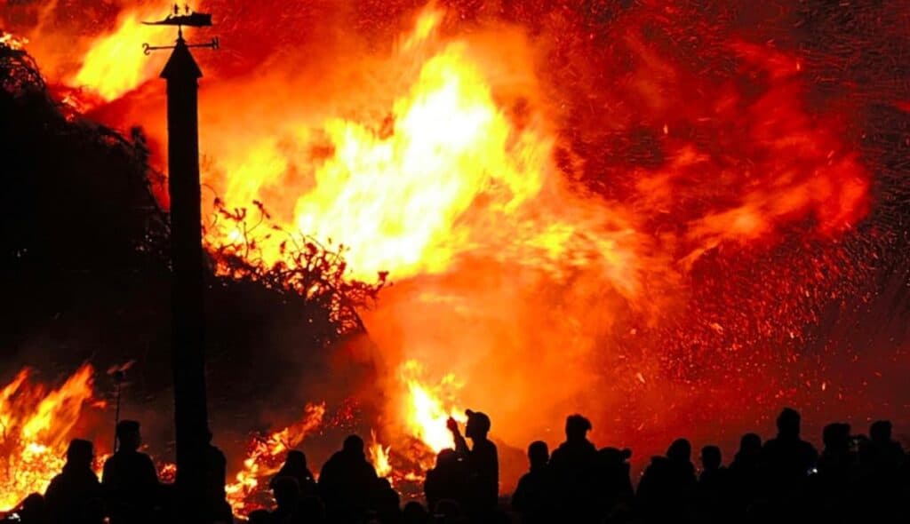 Grande falò notturno con folla di spettatori.