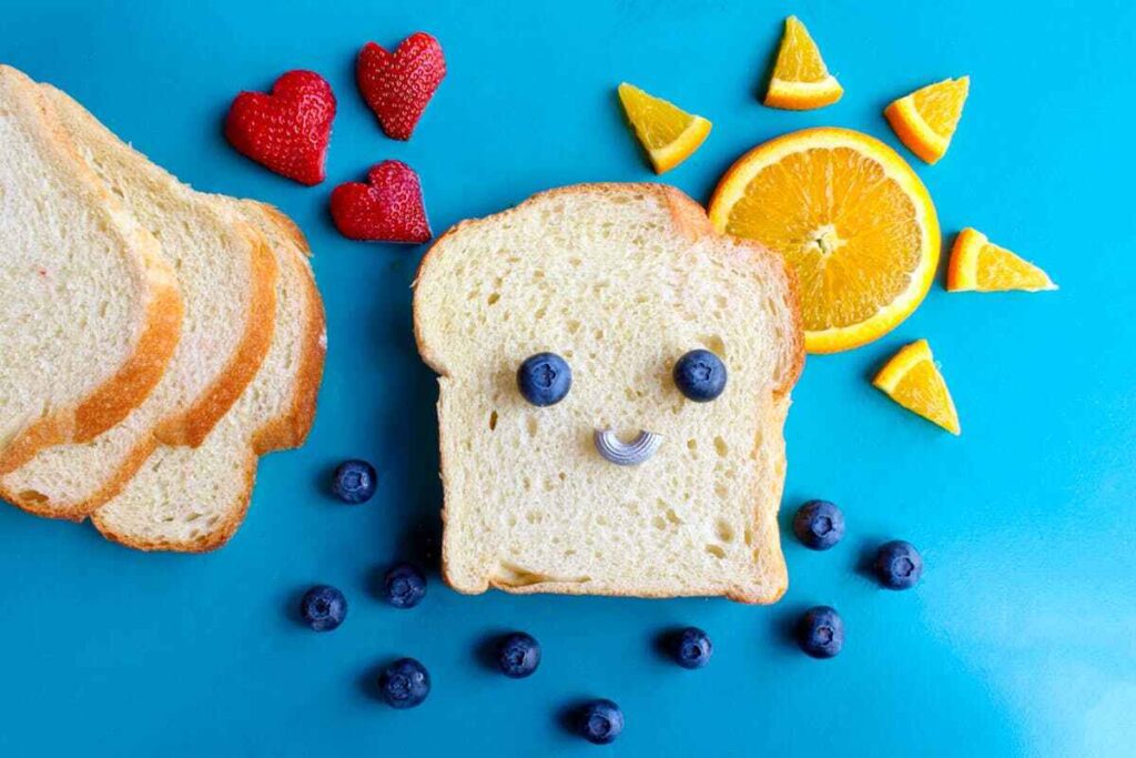 Fetta di pane con frutta a forma di viso sorridente.