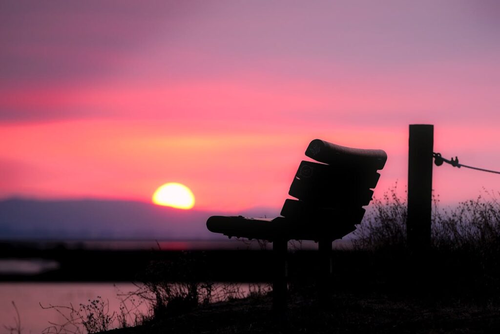 Arredamento urbano autocostruito: una seduta in legno rivolta verso il tramonto